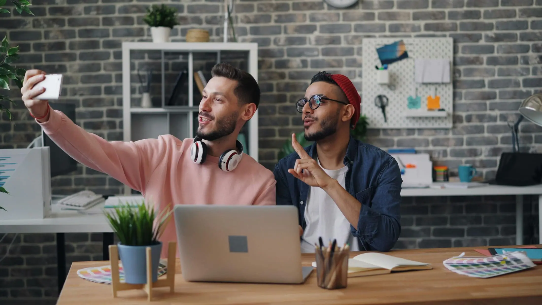 Two people taking a work selfie beside a laptop